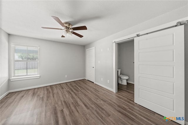 unfurnished bedroom featuring ceiling fan, a barn door, baseboards, and wood finished floors