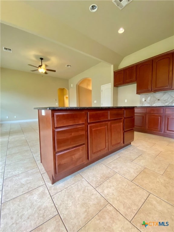 kitchen featuring ceiling fan, dark stone countertops, backsplash, and a kitchen island