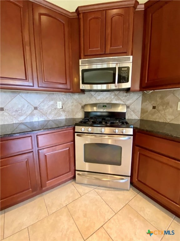 kitchen featuring decorative backsplash, appliances with stainless steel finishes, light tile patterned flooring, and dark stone countertops