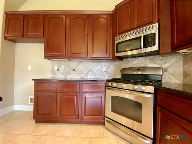 kitchen with appliances with stainless steel finishes, dark stone counters, backsplash, and light tile patterned flooring