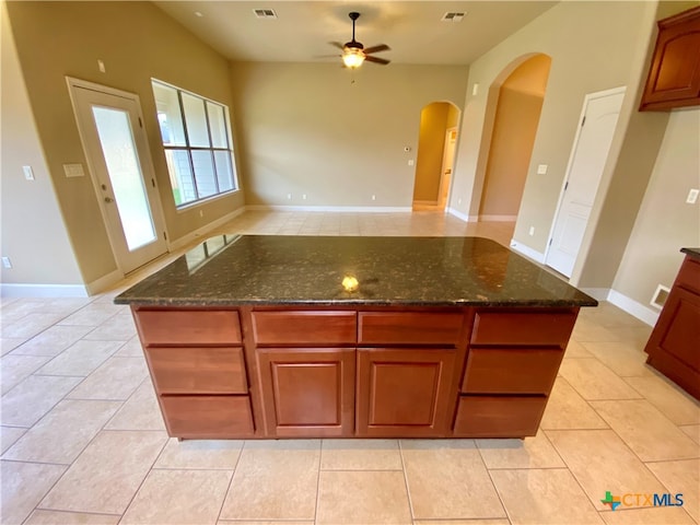 kitchen with dark stone counters, a kitchen island, light tile patterned floors, and ceiling fan