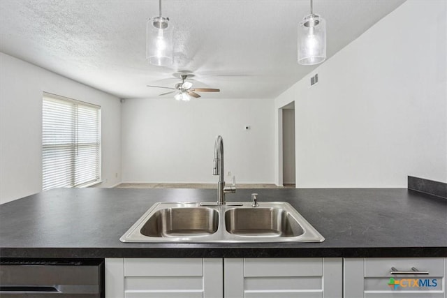 kitchen featuring a sink, dark countertops, dishwashing machine, and white cabinets