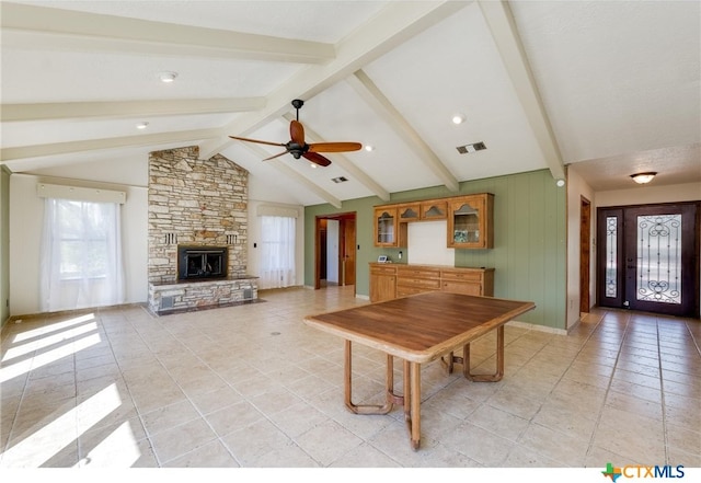 unfurnished dining area featuring lofted ceiling with beams, ceiling fan, a stone fireplace, light tile patterned floors, and visible vents