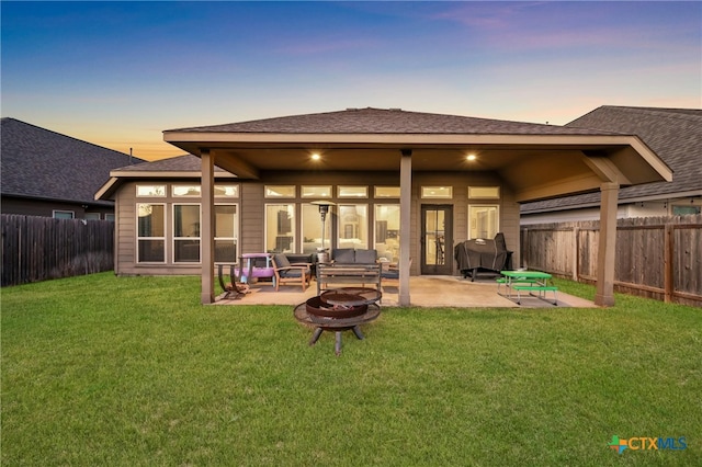 back house at dusk with a fire pit, a lawn, and a patio area