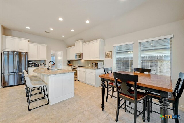 kitchen with stainless steel appliances, a sink, tasteful backsplash, white cabinetry, and a kitchen island with sink