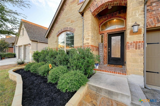 entrance to property featuring brick siding, stone siding, and roof with shingles