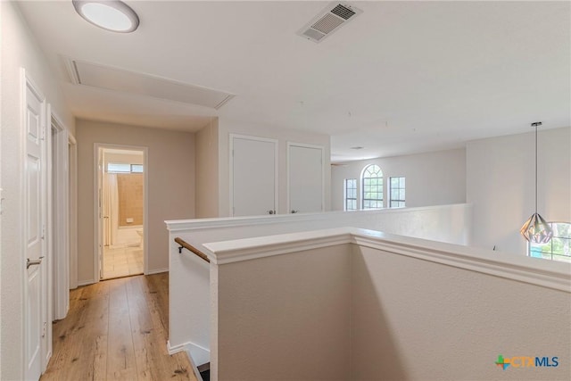 corridor featuring attic access, visible vents, light wood-type flooring, baseboards, and an upstairs landing