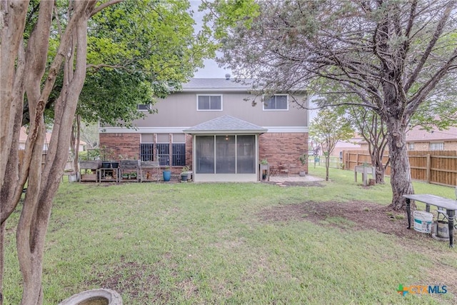 back of house featuring a lawn, brick siding, fence, and a sunroom