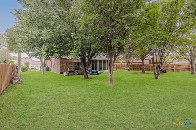 view of yard with central AC unit, a fenced backyard, and a sunroom