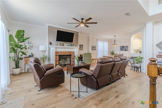 living room with crown molding, a ceiling fan, a brick fireplace, and light wood-type flooring