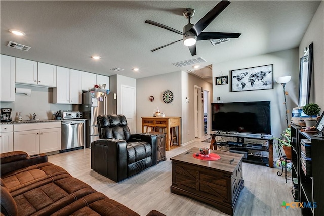 living room with ceiling fan, sink, a textured ceiling, and light hardwood / wood-style flooring