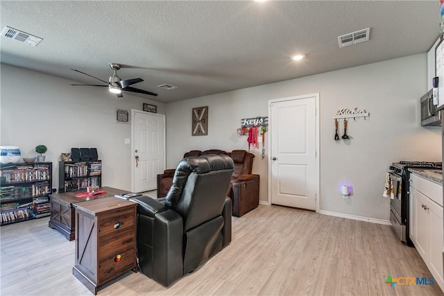 living room featuring ceiling fan, a textured ceiling, and light wood-type flooring