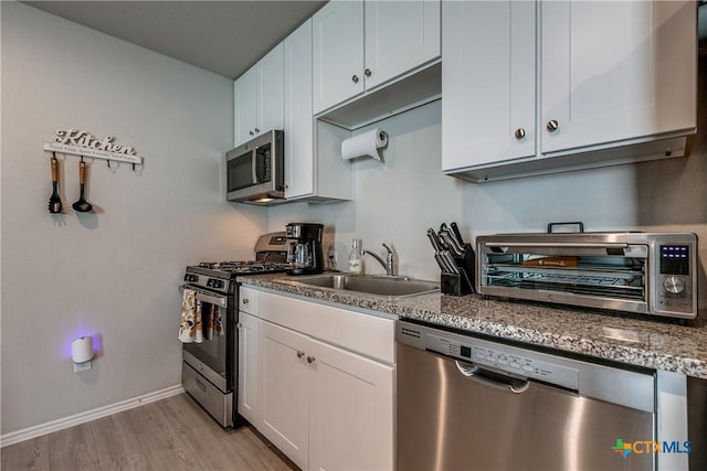 kitchen featuring sink, stainless steel appliances, white cabinets, stone countertops, and light wood-type flooring