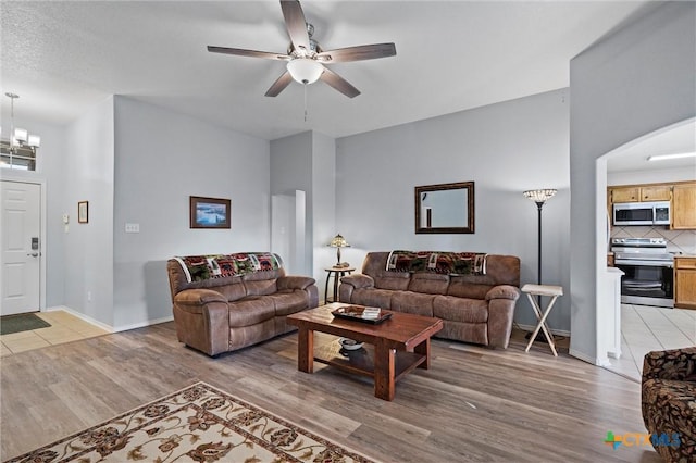 living room featuring ceiling fan with notable chandelier, baseboards, and light wood-style floors