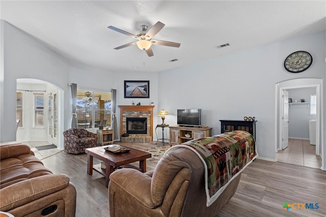 living room with arched walkways, a brick fireplace, a ceiling fan, and wood finished floors