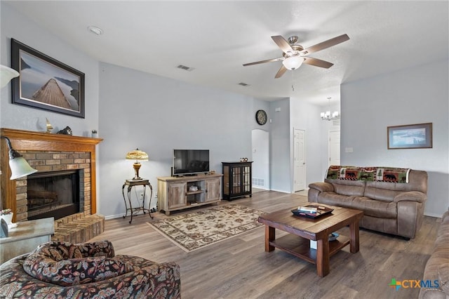 living room with wood finished floors, visible vents, baseboards, a fireplace, and ceiling fan with notable chandelier