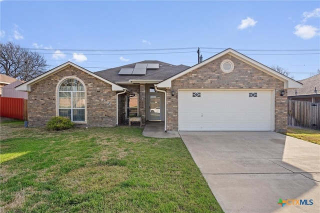 ranch-style home featuring an attached garage, a front lawn, concrete driveway, brick siding, and roof mounted solar panels