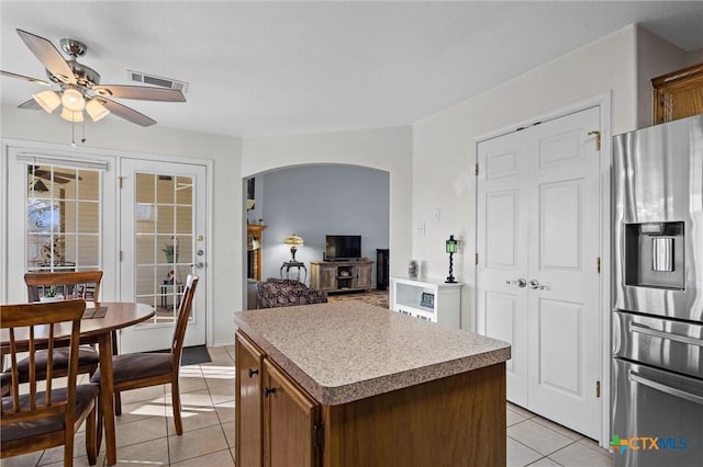 kitchen featuring a ceiling fan, visible vents, light tile patterned flooring, arched walkways, and stainless steel fridge