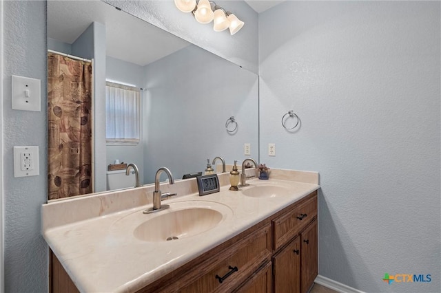 full bath featuring double vanity, a textured wall, and a sink