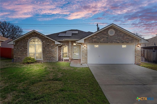 ranch-style house with roof mounted solar panels, fence, concrete driveway, an attached garage, and a front yard