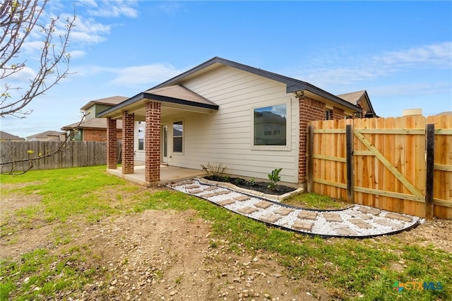 back of house featuring brick siding, fence private yard, a yard, a patio area, and a gate