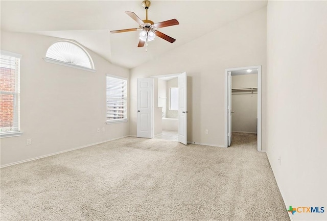 unfurnished bedroom featuring baseboards, ceiling fan, a walk in closet, light colored carpet, and connected bathroom