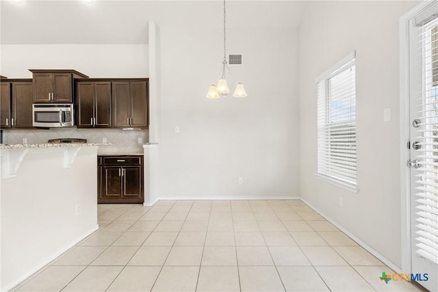 kitchen with visible vents, dark brown cabinetry, stainless steel microwave, tasteful backsplash, and a chandelier