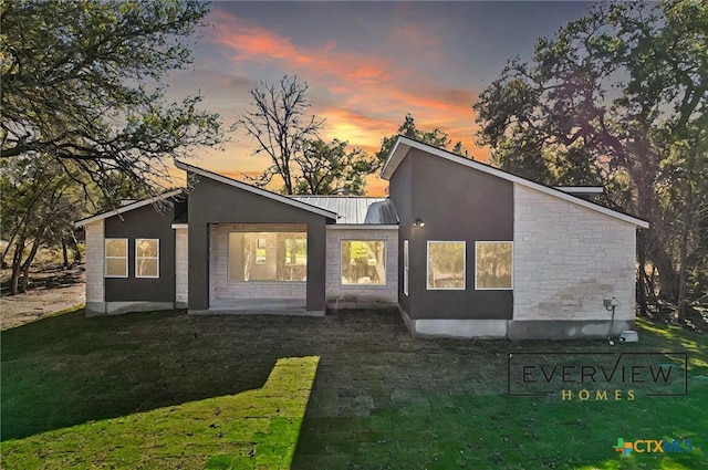 3006 Dew Drop, Horseshoe Bay, TX 78657 - back of house at dusk with a standing seam roof, metal roof, stucco siding, stone siding, and a lawn