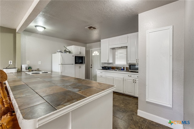 kitchen with white fridge, white cabinetry, a textured ceiling, tile counters, and black microwave