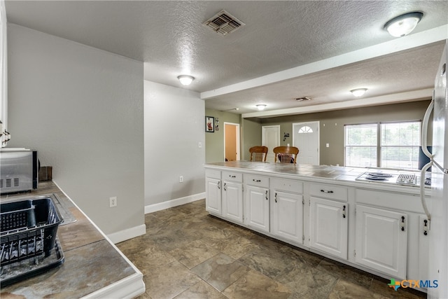 kitchen featuring tile countertops, white appliances, a textured ceiling, and white cabinets