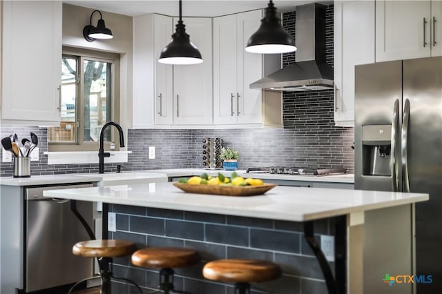 kitchen with appliances with stainless steel finishes, backsplash, wall chimney range hood, white cabinetry, and hanging light fixtures