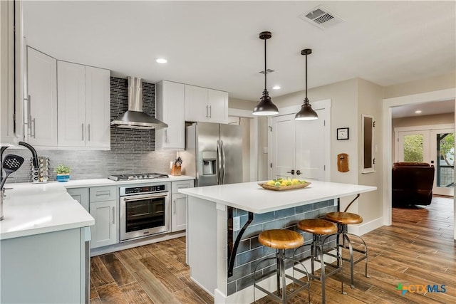 kitchen with wall chimney exhaust hood, stainless steel appliances, decorative light fixtures, decorative backsplash, and a kitchen island