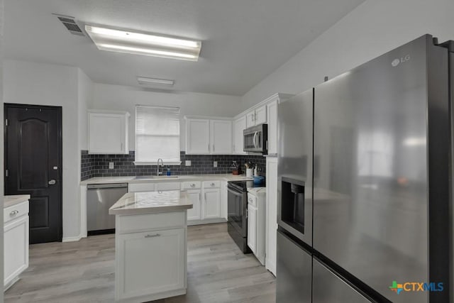 kitchen with stainless steel appliances, a kitchen island, sink, light hardwood / wood-style floors, and white cabinetry