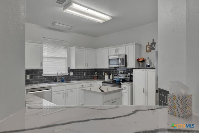 kitchen featuring decorative backsplash, appliances with stainless steel finishes, light stone countertops, sink, and white cabinetry