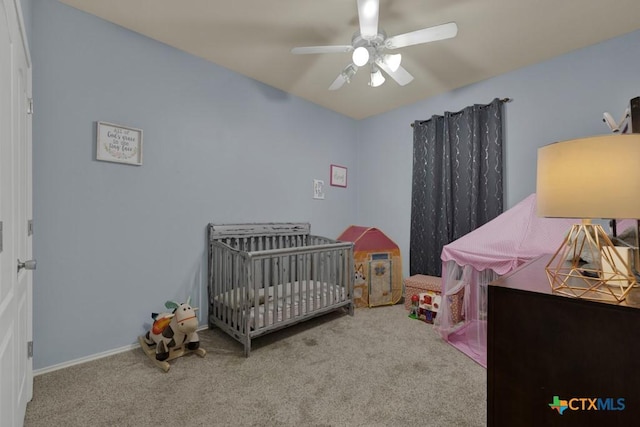 carpeted bedroom featuring ceiling fan and a nursery area