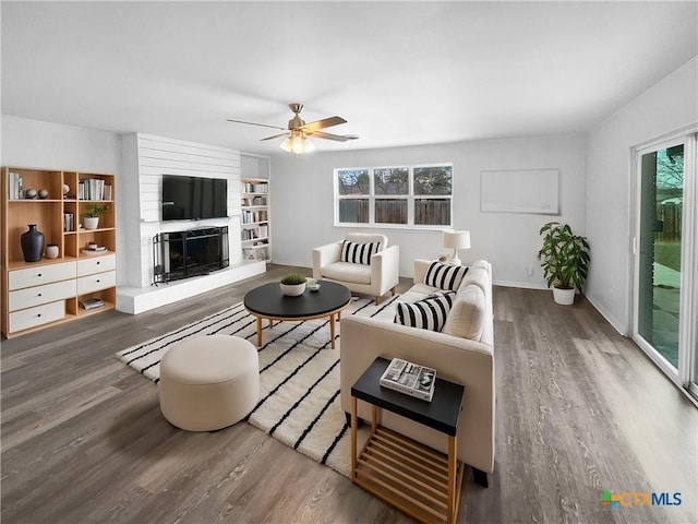 living room with a fireplace, ceiling fan, and dark wood-type flooring