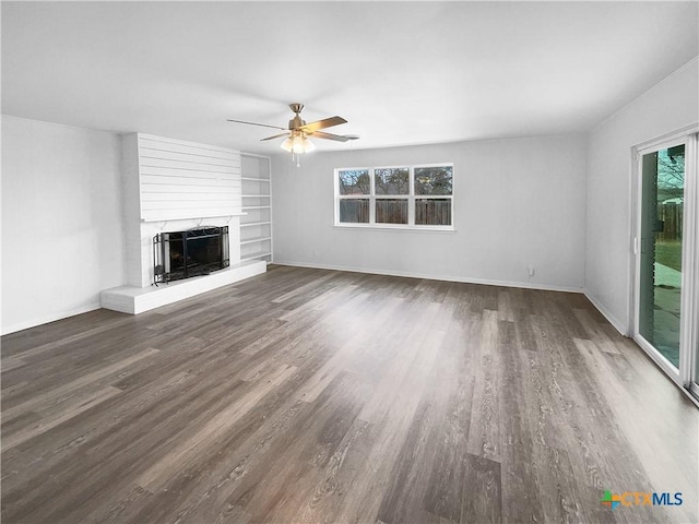 unfurnished living room featuring ceiling fan, a large fireplace, a wealth of natural light, and dark wood-type flooring