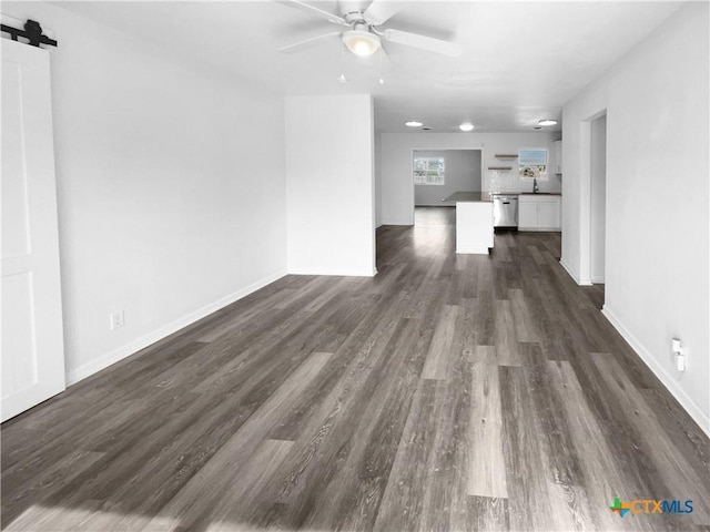 unfurnished living room featuring ceiling fan, a barn door, dark hardwood / wood-style flooring, and sink