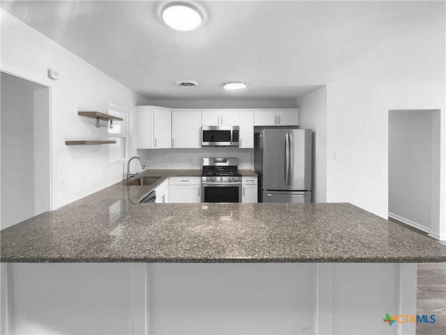 kitchen with kitchen peninsula, white cabinetry, dark stone counters, appliances with stainless steel finishes, and sink