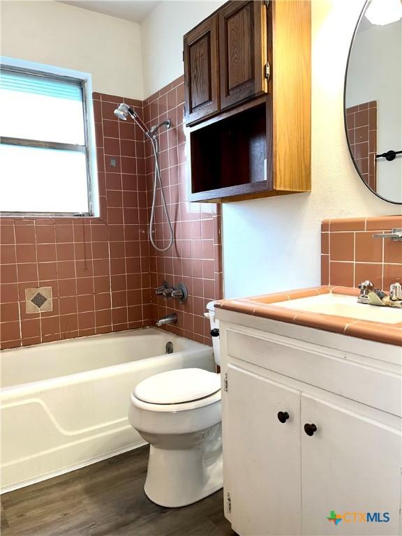 full bathroom featuring hardwood / wood-style floors, vanity, tiled shower / bath, decorative backsplash, and toilet