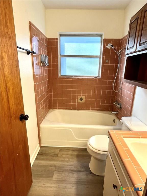 full bathroom featuring tiled shower / bath combo, toilet, wood-type flooring, and vanity