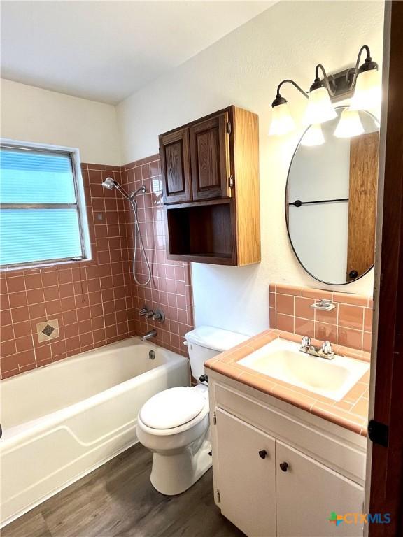 full bathroom featuring backsplash, vanity, tiled shower / bath combo, hardwood / wood-style floors, and toilet