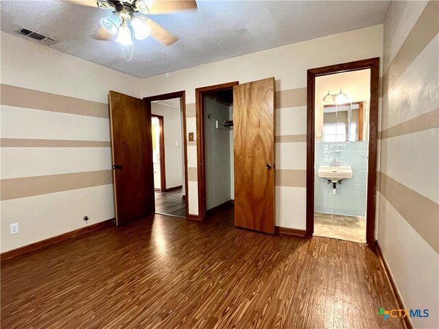 unfurnished bedroom with ceiling fan, sink, dark wood-type flooring, ensuite bathroom, and a textured ceiling