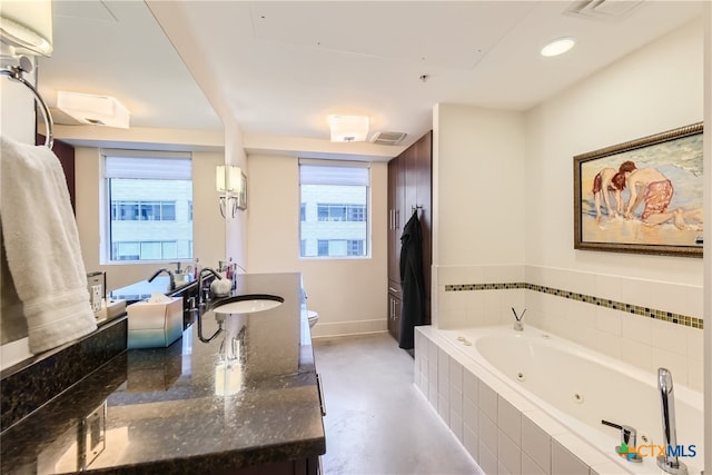 bathroom with a relaxing tiled tub, vanity, and toilet