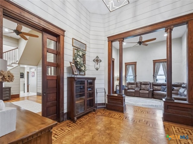 interior space with a towering ceiling, wood walls, ceiling fan, and ornate columns