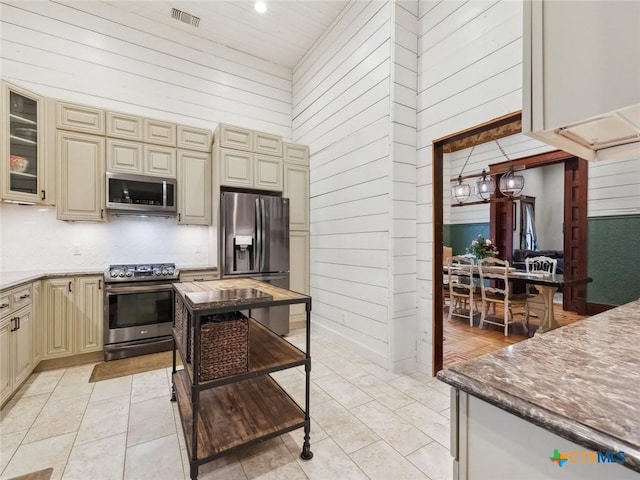 kitchen featuring light tile patterned flooring, appliances with stainless steel finishes, light stone counters, and cream cabinetry