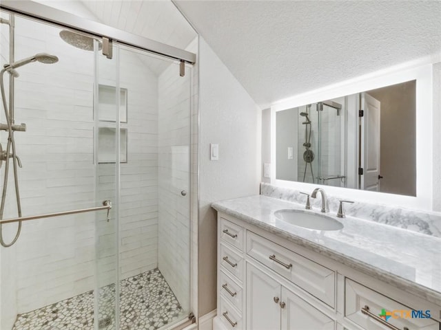 bathroom featuring vanity, lofted ceiling, a textured ceiling, and a shower with shower door