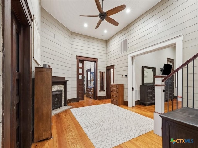 foyer entrance featuring hardwood / wood-style flooring, a fireplace, wooden walls, and ceiling fan