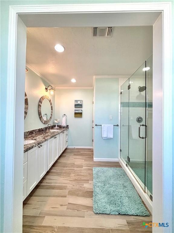 bathroom featuring double vanity, visible vents, ornamental molding, a stall shower, and wood finished floors