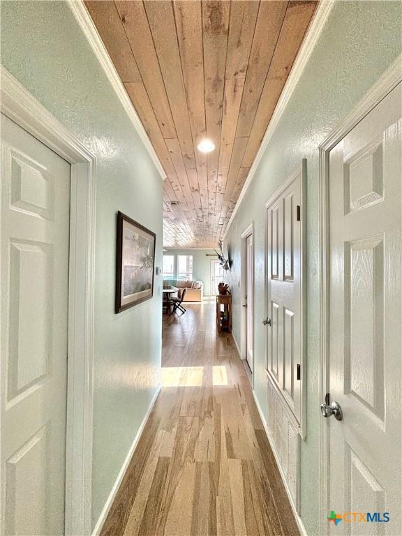 hall with ornamental molding, wooden ceiling, baseboards, and wood finished floors